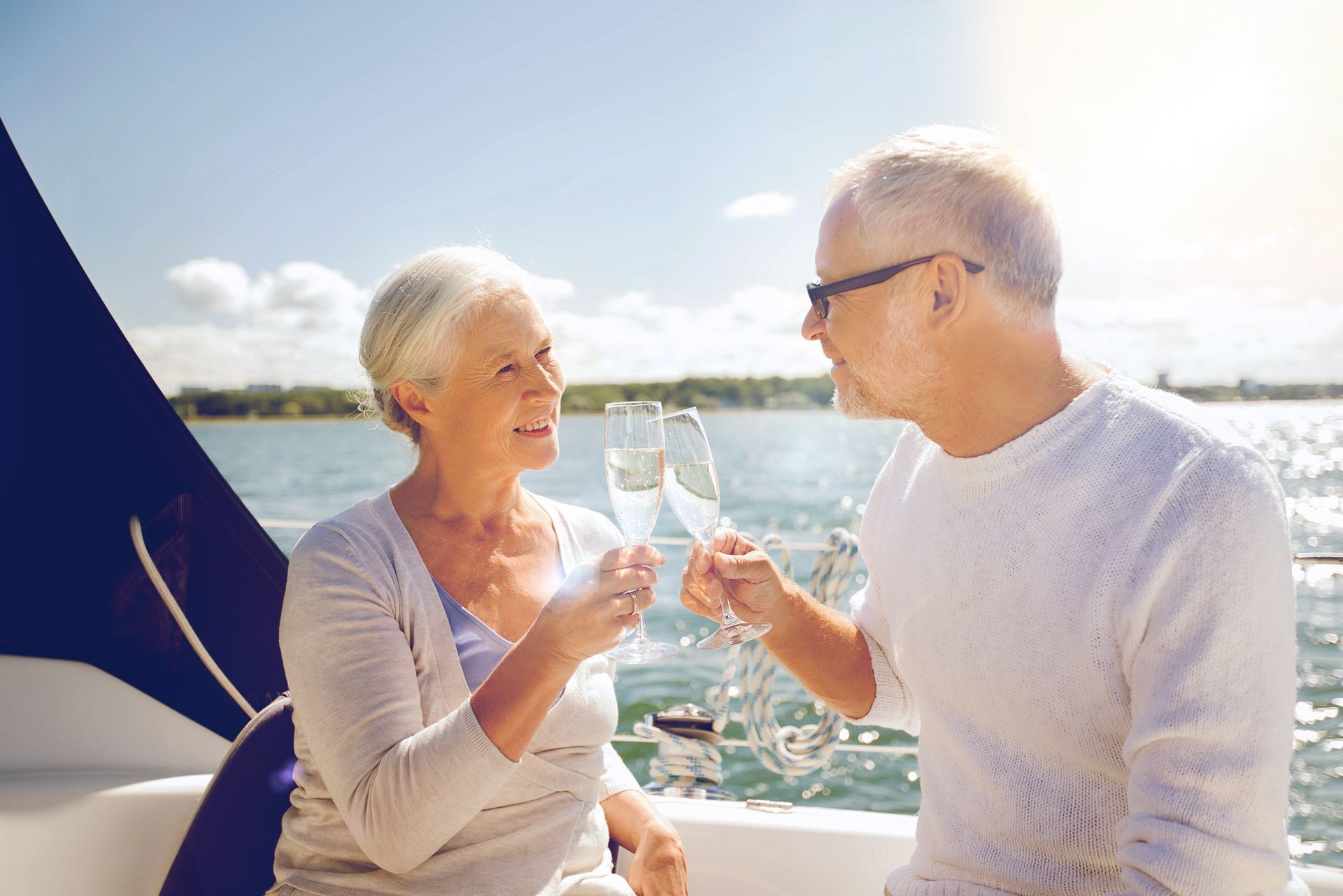 sailing, age, travel, holidays and people concept - happy senior couple clinking champagne glasses on sail boat or yacht deck floating in sea